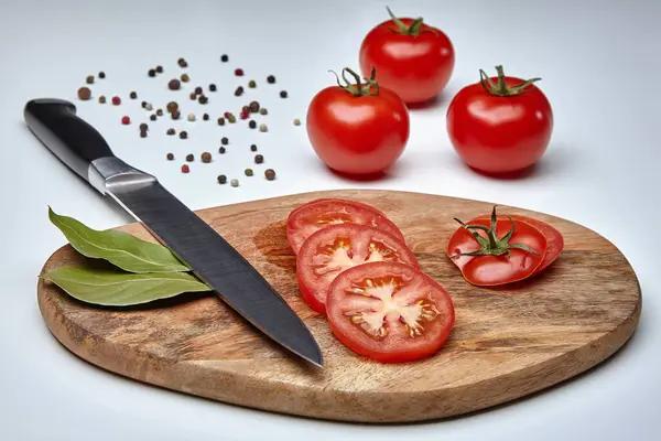 Kesme tahtasındaki olgun domatesler, yanında bir bıçak ve üç domates.