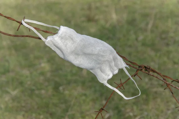 White virus protection mask hanging on a rusty barbed wire