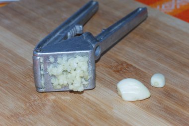 Sarımsak ezicisi, ahşap bir tahta üzerinde sarımsaklı karanfil.