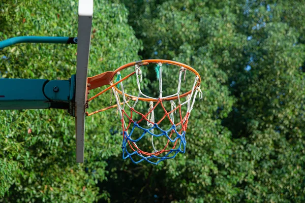 basketball hoop with colored net against a blue sky with white clouds
