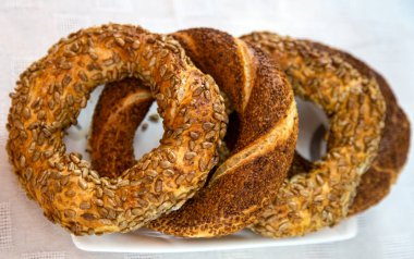 Beyaz tabakta ve beyaz masa örtüsünde yan yana simitler. 