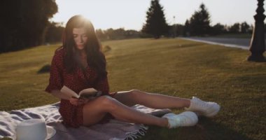 Güzel kız yaz günbatımında çimlerin üzerinde otururken bir kitap okur. Sundress giymiş güzel bir kadın parkta oturur ve şiir okur. Genç dişi güneşin altında dışarıda ders çalışıyor. Açık hava eğlencesi 