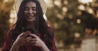Sundress 'li tatlı kız gün batımında parkta bir mesaj yazıyor. Güneşin altında akıllı telefonlu güzel bir kadın.
