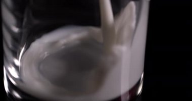Süt yavaş çekimde siyah bir arka planda bir bardağa dökülüyor.