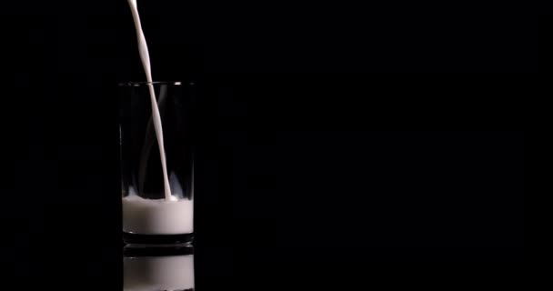 le lait en gros plan est versé dans un verre sur un fond noir au ralenti 