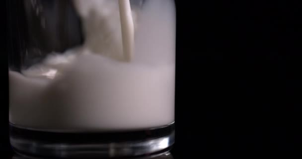 Macro éclaboussures de lait verser dans un verre sur un fond noir au ralenti 