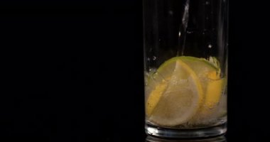 Limonlu soda ve limonlu suyu yavaş çekimde siyah arka plana dök. Buzlu limonata.