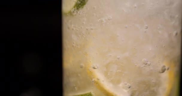 用柠檬和石灰在黑色背景上慢动作地把苏打水关上 杯子里的柠檬水 — 图库视频影像