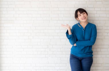 Güzel, genç Asyalı bir kadın ayakta ve gülümsüyor mutlu ve bir şeyler sunuyor ve geleceği gösteriyor ya da çimento arka plan, yaşam tarzı konsepti üzerine senin mesajınla plan yapıyor..