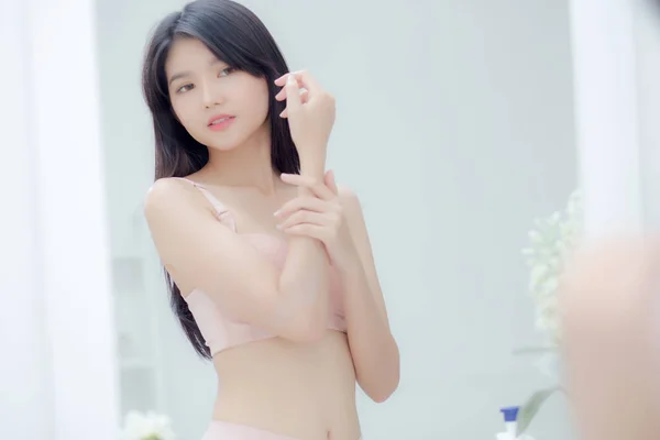 腕やメッセージにクリームを適用する鏡を探して美しいセクシーな若いアジアの女性 健康と柔らかい水分補給のためのボディローションスキンケアを適用する美少女 保湿剤で治療と化粧品 — ストック写真