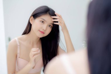 Gülümseyen genç Asyalı bir kadın odadaki dokunmatik saç aynasına, hijyen için makyaj malzemesine, güzellik asyalı bir kız evde saç stili, yaşam tarzı ve makyaj konsepti için mutlu..