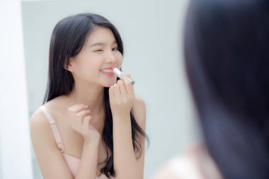 Güzel, genç Asyalı bir kadın ruj sürüyor. Pembe, tarzı parlak ve parlak dudakları var. Güzellik aynası arıyor..