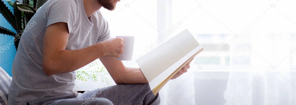 Young man reading a book sitting on sofa for rest is hobby in living room, stay home for leisure, lifestyle of new normal for social distracting, male learn and study in interesting in spare time.