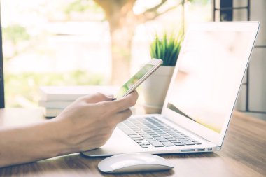 Evde çalışan iş adamı dizüstü bilgisayarla masadaki interneti kullanıyor, yeni normal, sosyal mesafeli yaşam tarzı, evde kalıp telefona ve iletişim konseptine bakıyor..