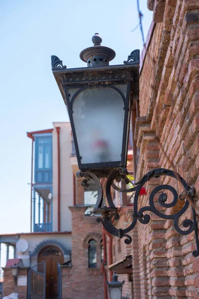 decorative wrought iron street lamp on the wall of a brick house