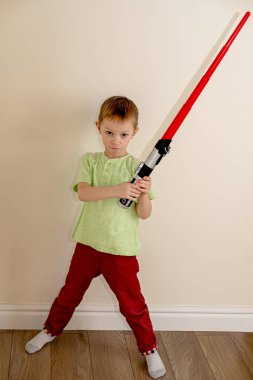 Şeytani yüzlü çocuk odada plastik bir ışın kılıcı tutuyor.
