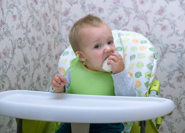 Niño pequeño en la cocina se sienta en una silla alta y se come un pedazo de manzana — Foto de Stock