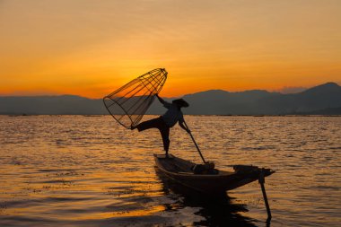 Inle Gölü, Myanmar. Bambu tekne turist için gün batımında poz Shan devlet Intha etnik gruptan Geleneksel giyimli balıkçı.