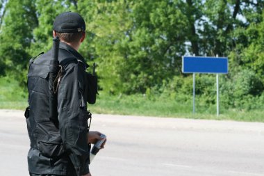 The officer inspects the road. The officer stands in black uniform with his back