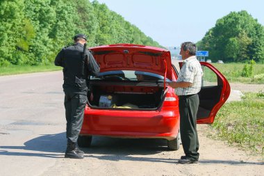Ukraine, May 27, 2011. An officer inspects the trunk of a red car. The driver is watching.