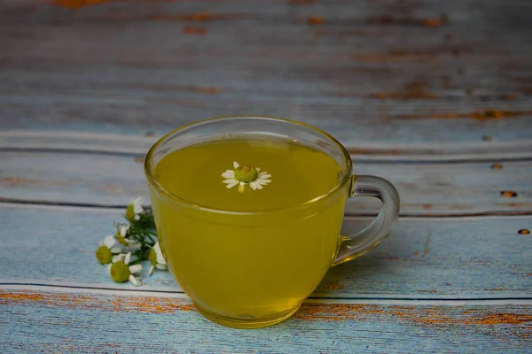 Thé aromatique chaud avec des fleurs de camomille dans une tasse en verre sur bois vintage — Photo