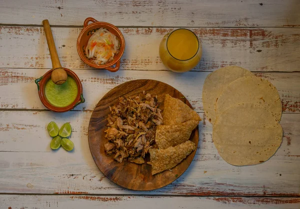 Tradycyjne danie meksykańskiej żywności na tacos carnitas wieprzowiny i tradycyjne danie meksykańskiej żywności na tacos carnitas wieprzowiny i wody aromatyzowanej, tortille, pikantny sos, cebula z chili, chicharron, cytryny o — Zdjęcie stockowe