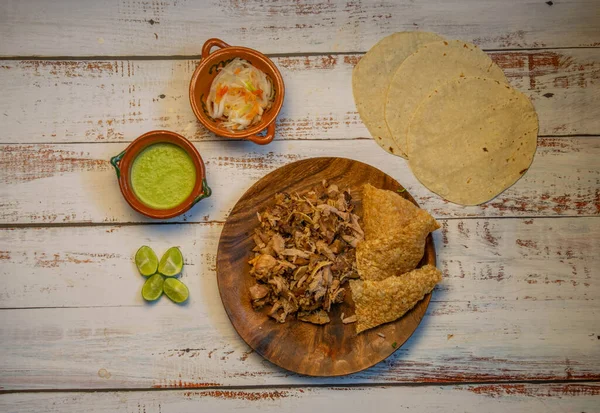 Plato tradicional de comida mexicana para tacos de carnitas de cerdo con tortillas, salsa picante, chicharrón, cebolla con chile, limones sobre una mesa de madera —  Fotos de Stock