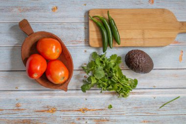 Domatesli, serrano biberli, kişniş ve avokadoyla lezzetli bir Meksika sosu hazırlamak için taze ve organik malzemeler. Hepsi eski mavi ahşap bir masada.