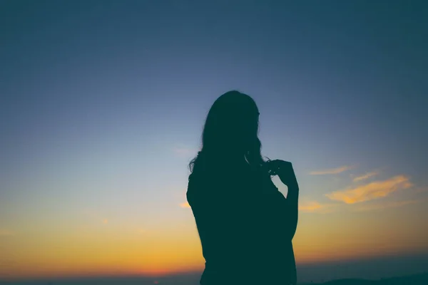 backlit silhouette of young woman posing at sunset of blue and red sky