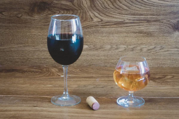 Composición de bebidas alcohólicas con copa de whisky y copa de vino tinto en el escenario de mesas de roble con un corcho de botella — Foto de Stock