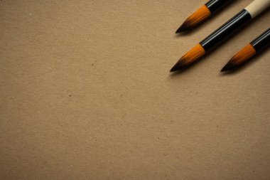 Eskiz yapmak için kahverengi boş bir kağıdın köşesinde tahta saplı üç adet sanat fırçası..