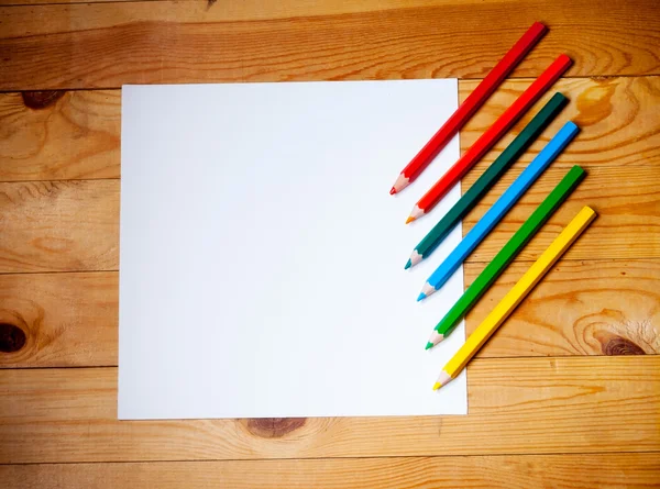 Papel em branco e lápis coloridos na mesa de madeira. Vista de cima — Fotografia de Stock