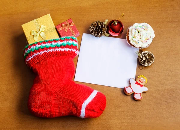 Christmas stocking with card, gifts, sweets and decorations  over wooden  background — Stock Photo, Image