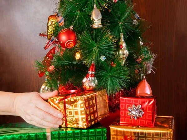 Kvinna hand sätta jul närvarande rutan under julgranen — Stockfoto
