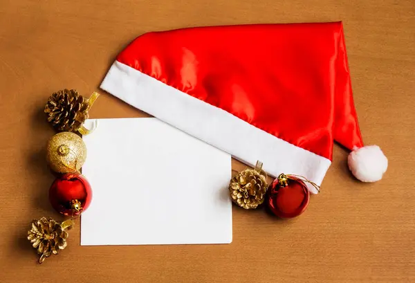 Vánoční karta s Santa čepice a vánoční ozdoby na dřevěné pozadí — Stock fotografie