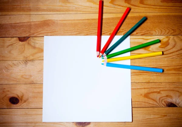 Papel en blanco y lápices de colores sobre el fondo de madera. Vista desde arriba —  Fotos de Stock