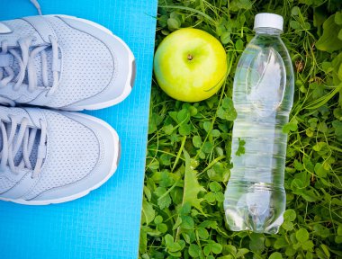 Yoga mat, şişe su ve taze yeşil çimenlerin üzerinde elma spor ayakkabı
