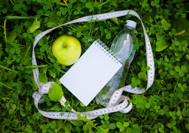 Şişe su, teyp ve elma yeşil çimenlerin üzerinde ölçüm