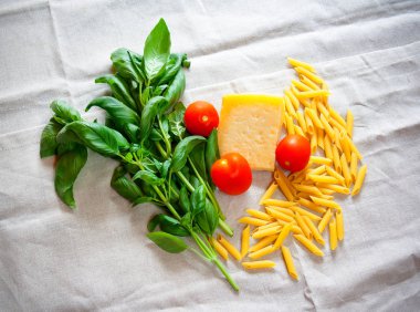 Fesleğen, domates, parmesan ve pişmemiş makarna penne gri masa örtüsü üzerinde