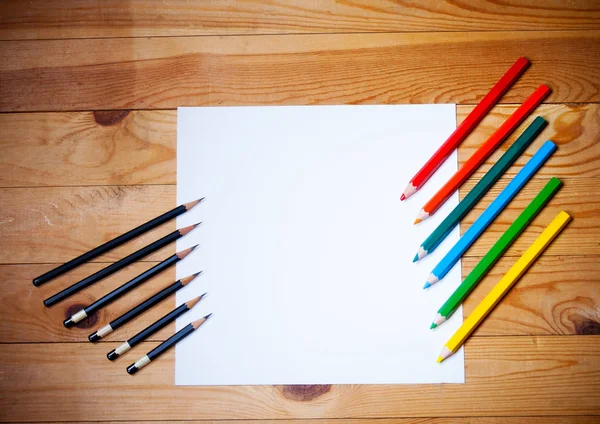 Papel em branco e grafite e lápis coloridos no fundo de madeira — Fotografia de Stock
