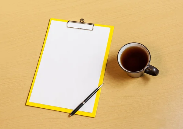 Urklipp med vitt ark, kopp te och penna på skrivbord — Stockfoto