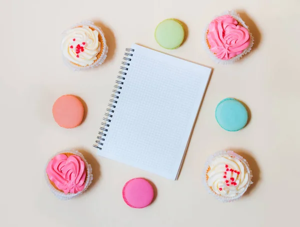 Γλυκό πολύχρωμα μακαρόν, cupcakes και σημειωματάριο σε μπεζ φόντο — Φωτογραφία Αρχείου