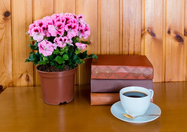 Libros, taza de café y flor de pelargonia sobre mesa de madera —  Fotos de Stock