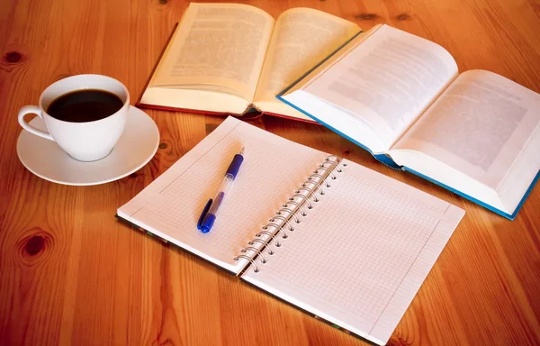 Böcker, tom anteckningsbok, penna och kopp kaffe på skrivbord — Stockfoto