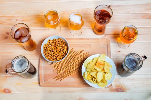 Cerveza sobre mesa de madera. Los bocadillos de cerveza son papas fritas, pajitas saladas y pretzels — Foto de Stock