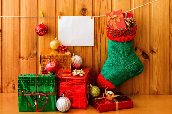 Christmas stocking, greeting card and presents against wooden wall — Stock Photo, Image