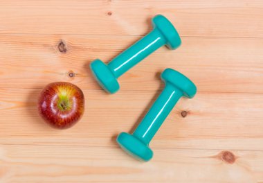 İki yeşil dumbell ve ahşap arka plan üzerinde elma 