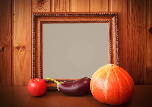 Fresh vegetables and picture frame on wooden background