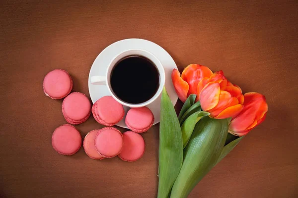 Tazza di caffè con amaretti rosa e fiori di tulipano su sfondo di legno — Foto Stock