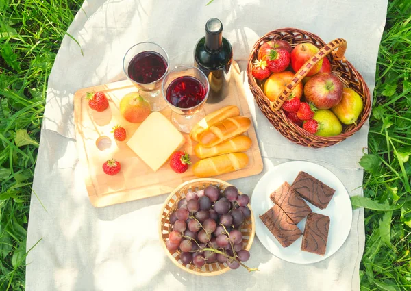 stock image Outdoor picnic setting with red wine, cheese, fruits and cakes. 